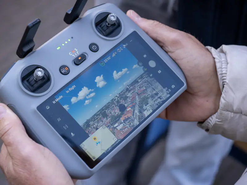 DJI-controller in de handen van een deelnemer, met live beeld vanuit de lucht: een stad met wolken boven de horizon (foto: Arne Wessels)