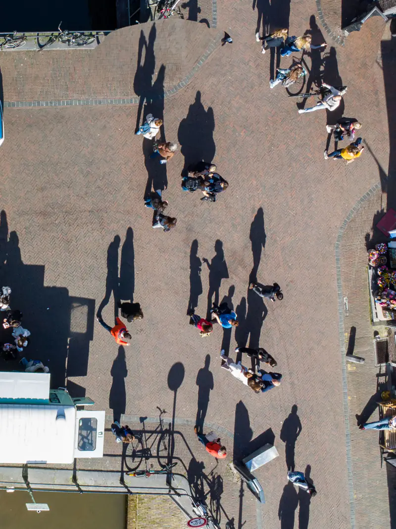 Mensen met lange schaduwen op een plein in Utrecht, recht van boven