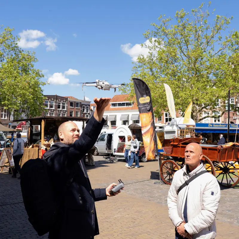 De drone stijgt op vanaf de hand op een marktplein, tijdens een workshop dronevliegen