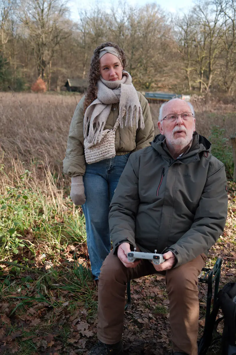 Opa zit met de controller op schoot, zijn kleindochter staat achter hem