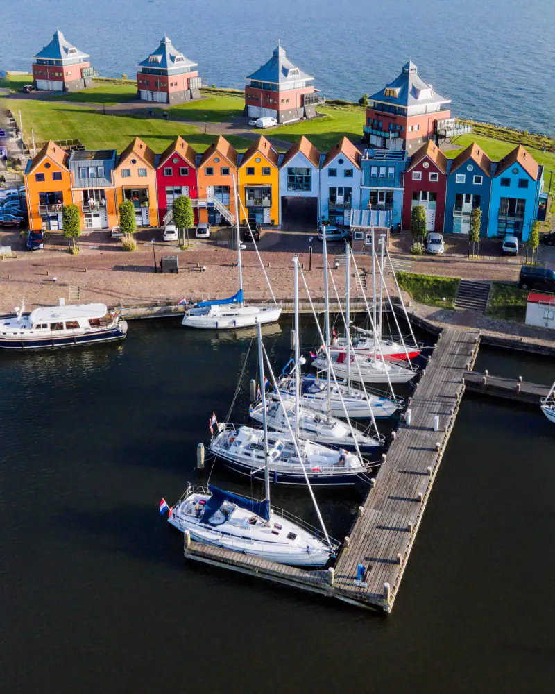 Rij gekleurde huizen aan een jachthaven met zeilboten, vanuit de drone
