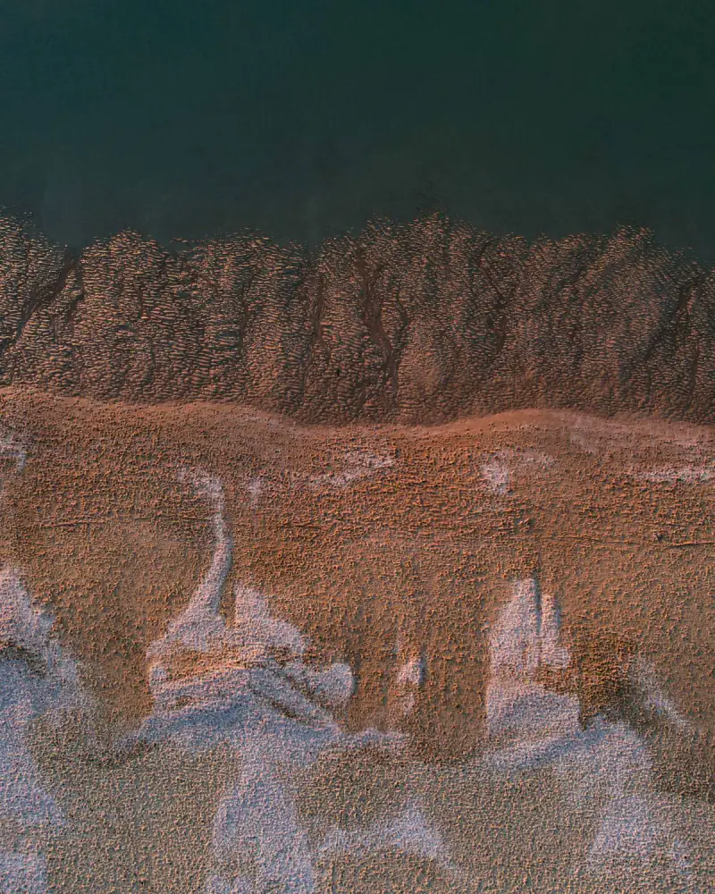 Het Haagse strand recht van boven: zee, zandribbels en schelpen in het avondlicht