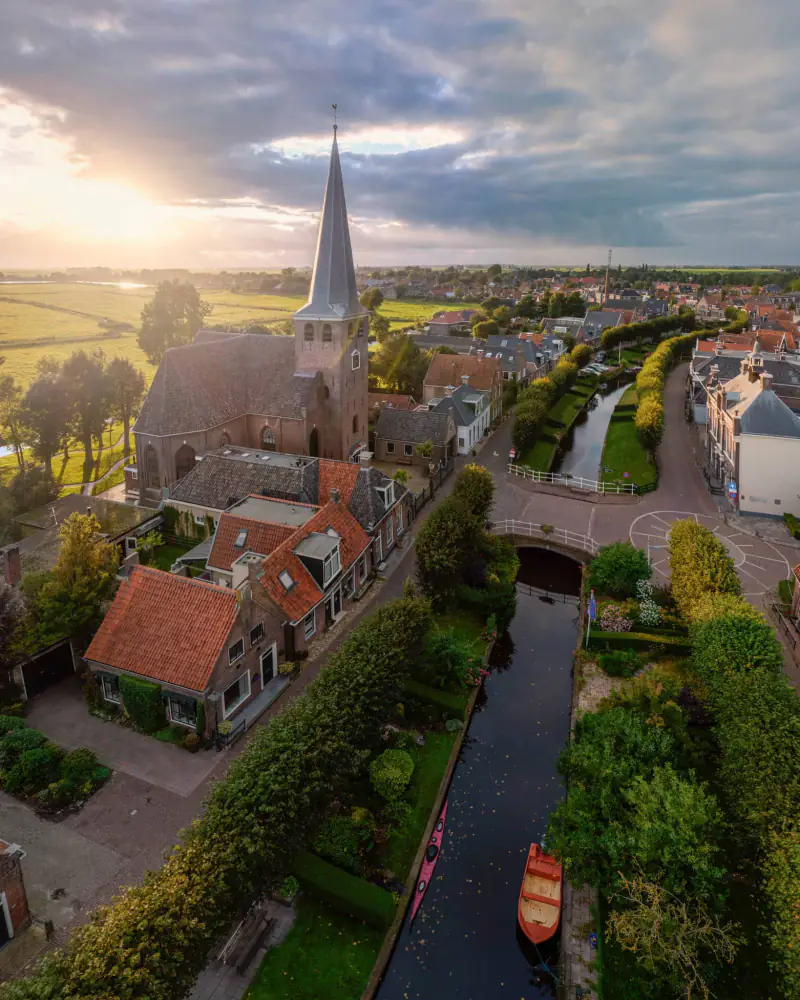 Kerk met spitse toren aan een gracht met een kano en een roeiboot, in het eerste zonlicht