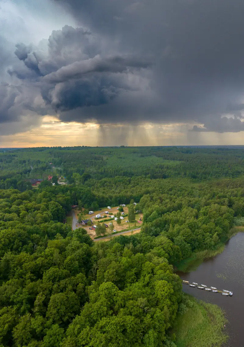 Onweersbui met regenstrepen boven bos, een camping en een meer in Zweden, vanuit de drone