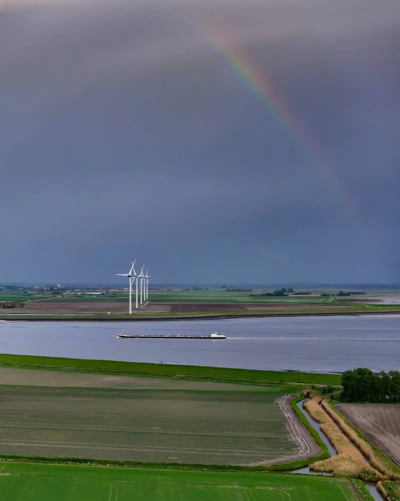 Regenboog boven windmolens en een binnenvaartschip op het water, vanuit de drone