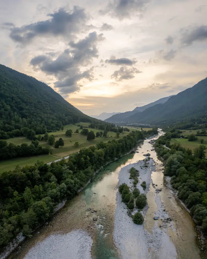 Brede rivier met grindbanken door een groen bergdal in Slovenië, vanuit de drone