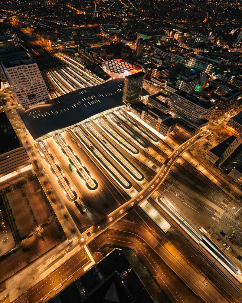 Station met perronkappen en verlichte straten bij nacht, vanuit de drone