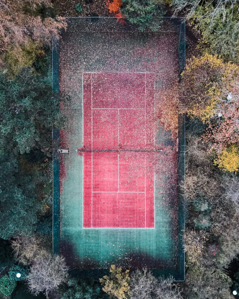 Rode tennisbaan tussen herfstbomen, recht van boven