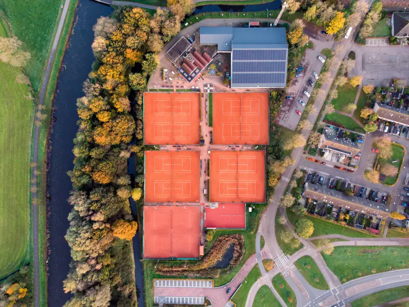 Tennispark met rode banen tussen herfstbomen, recht van boven